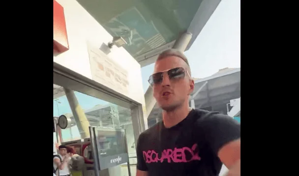 Чоловік з ірокезом у сонцезахисних окулярах і чорній футболці DSQUARED2 біля скляних дверей