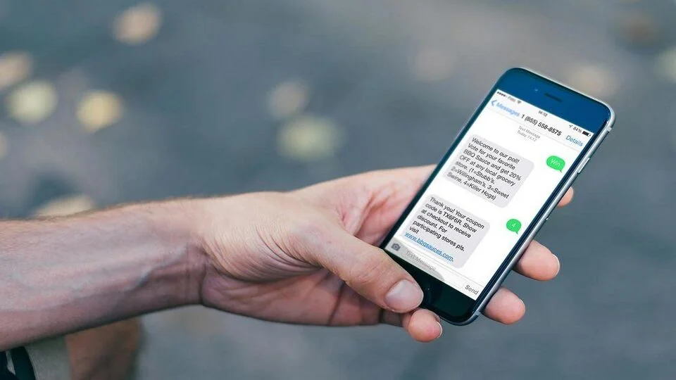 Рука тримає смартфон з небезпечним SMS-повідомленням про акції, купони та посилання на bhbsauces.com alt: Рука тримає смартфон з небезпечним SMS-повідомленням про акції, купони та посилання на bhbsauces.com