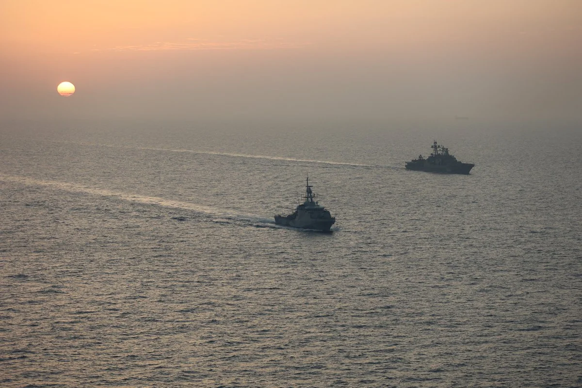 Два військові кораблі пливуть морем на заході сонця
